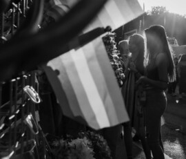 flag and lensflare Mittig im Bild die Regenbogen Flagge an einem Verkaufsstand. Hintergrund Silhouetten von Personen und lensflare